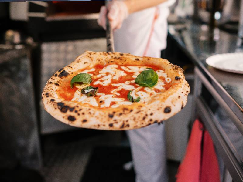 Larry's Pizza - Pizzabäcker hält frisch gebackene Pizza in die Kamera
